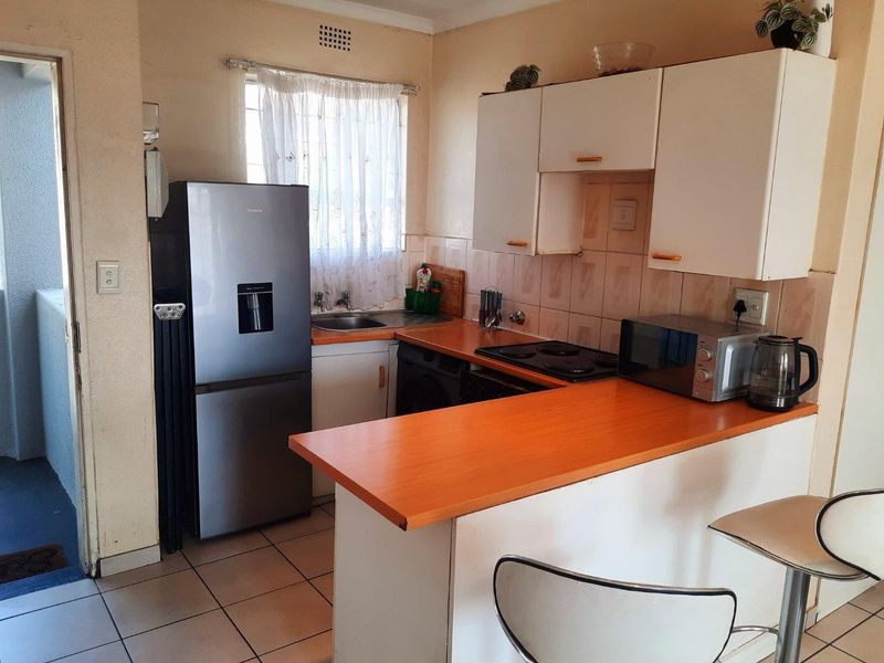 A compact kitchen featuring built-in cabinetry, laminate countertops, an electric hob, and tiled flooring, offering a functional layout for daily use.