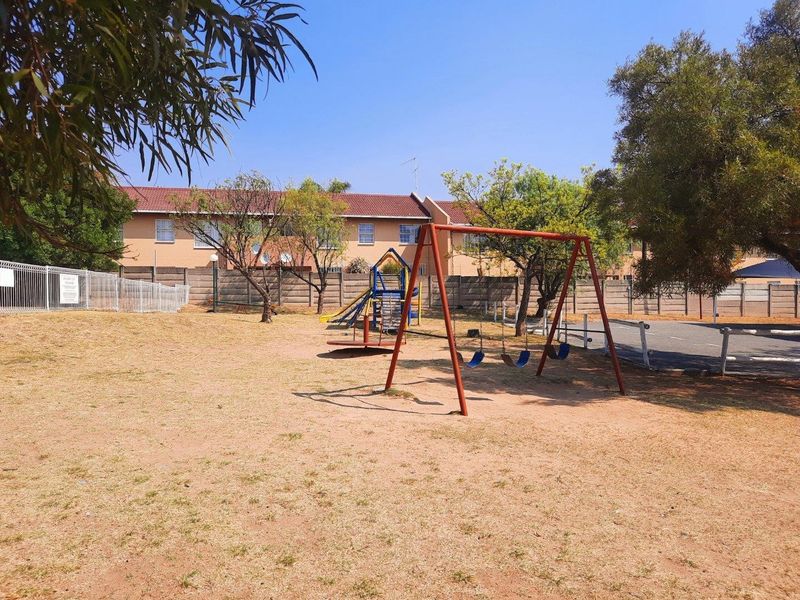 Communal garden area featuring a playground with swing set and slide, enclosed by perimeter walls and fencing.