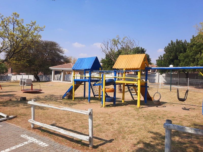 A communal outdoor playground area featuring fixed play structures, swings, and a wooden perimeter fence within an apartment complex.