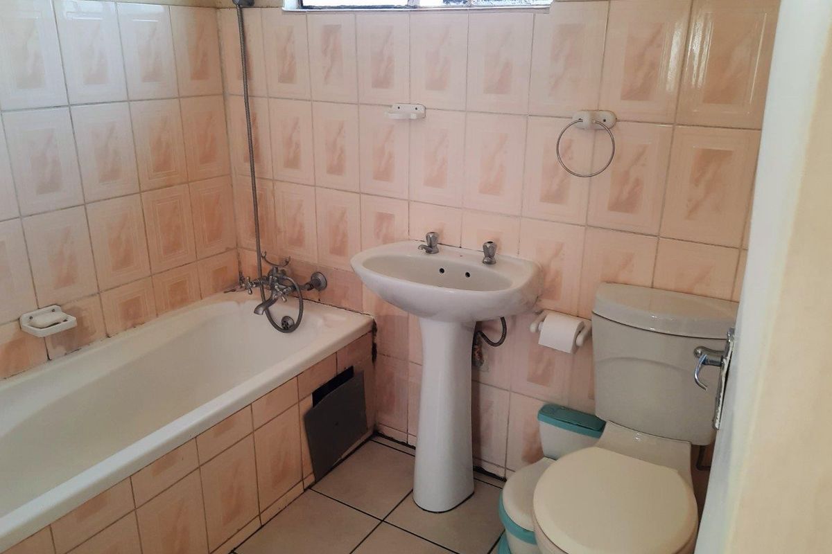 A dated bathroom featuring a pedestal basin, bathtub with shower mixer, and toilet, finished with original ceramic wall and floor tiling.