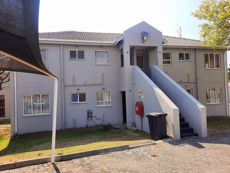 Exterior view of a multi-story apartment building featuring a tiled roof, external staircase access, and paved driveway area.