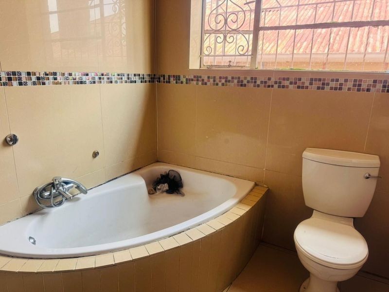A dated bathroom featuring a built-in corner bathtub, standard toilet, and tiled walls with decorative mosaic accents.