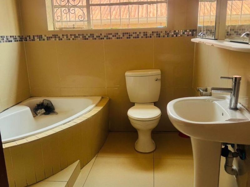A functional bathroom featuring a corner bathtub, pedestal sink, and toilet with neutral wall and floor tiling.