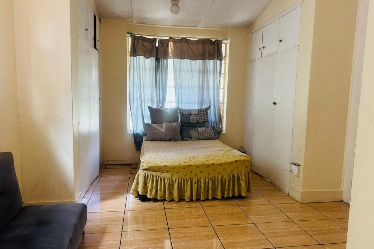 A bedroom featuring tiled flooring and built-in cupboards on either side of the window, providing functional storage space.