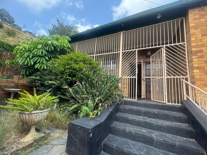 Front entrance of the house featuring brick facade, stone steps with metal railings, and a full-height security gate.