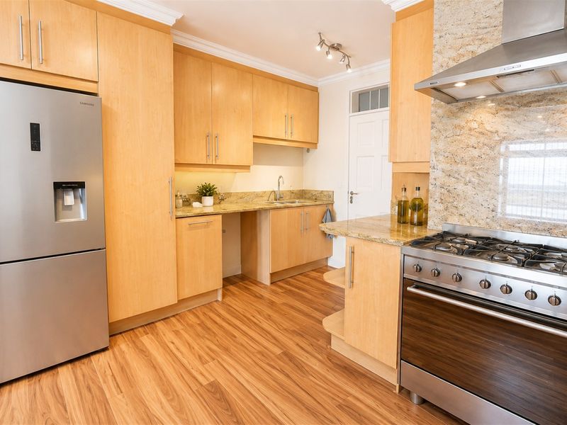 A well-maintained kitchen featuring light wood cabinetry, granite countertops, and a stainless steel gas stove with an extractor fan.