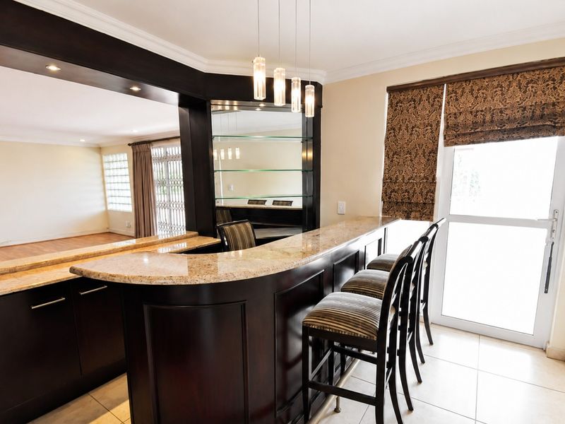 A well-appointed built-in home bar featuring dark wood cabinetry, granite countertops, mirrored shelving, and elegant pendant lighting, with direct access to the exterior.