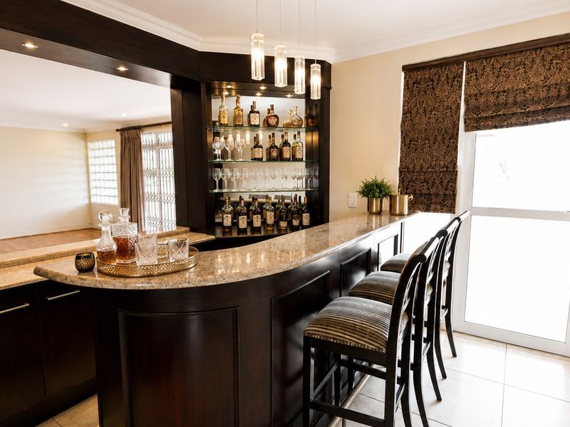 A well-appointed built-in home bar featuring dark wood cabinetry, granite countertops, glass shelving, and elegant pendant lighting.