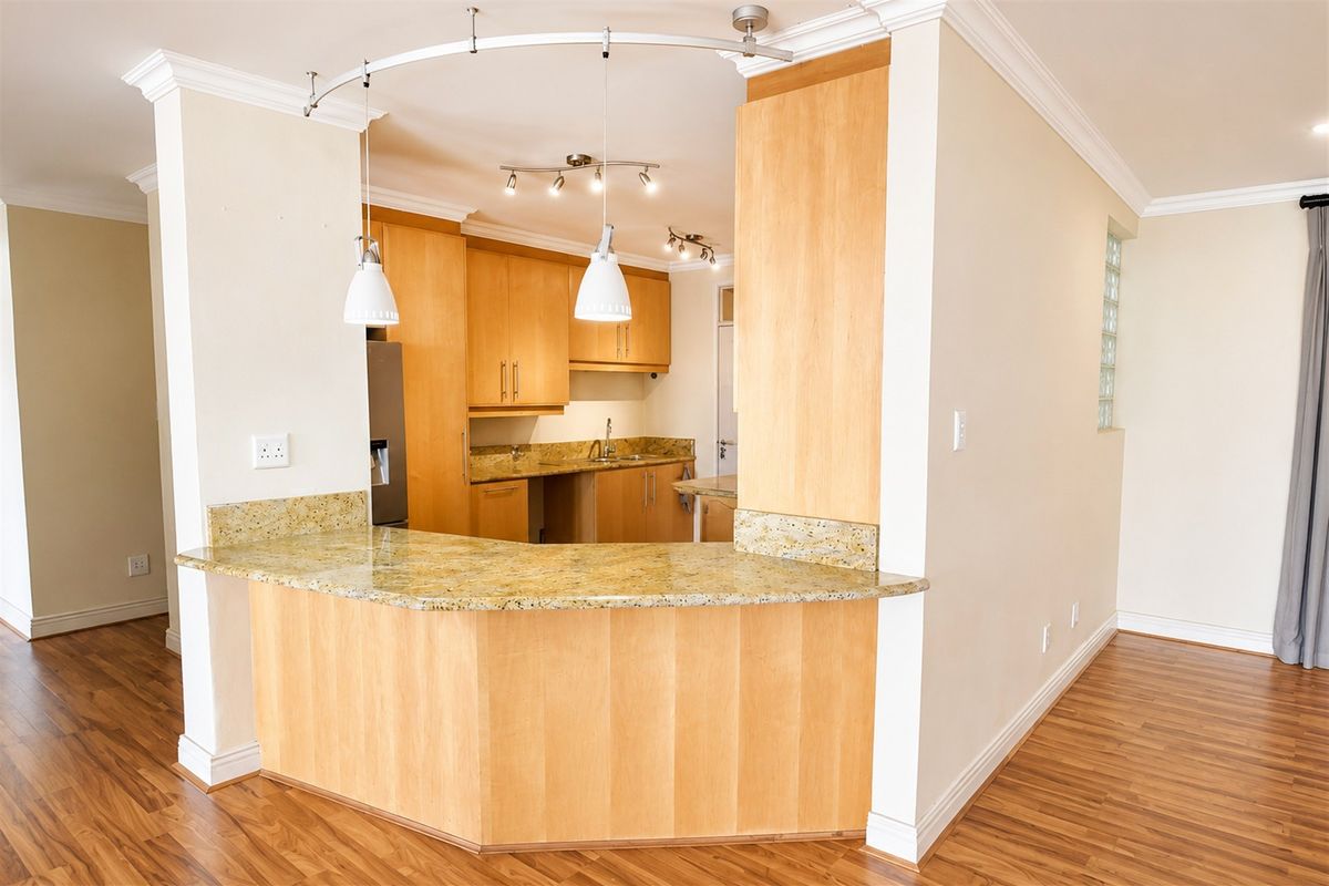 A functional kitchen featuring light wood cabinetry, granite countertops, and a breakfast bar, finished with laminate flooring and decorative cornice detailing.