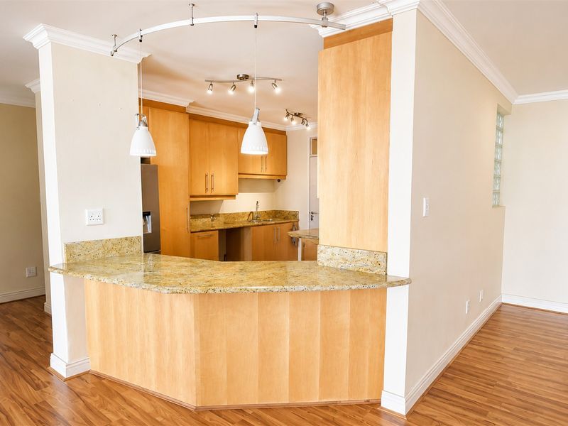 A functional kitchen featuring light wood cabinetry, granite countertops, and a breakfast bar, finished with laminate flooring and decorative cornice detailing.