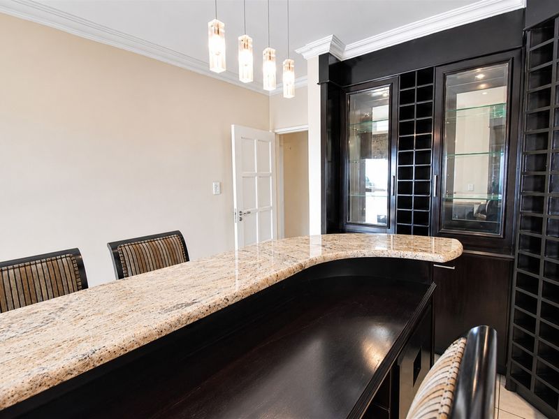 A sophisticated built-in bar area featuring a granite countertop, custom dark wood cabinetry with integrated wine storage, and elegant pendant lighting.
