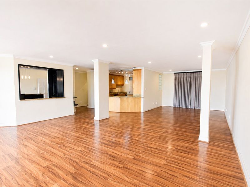 Spacious open-plan living and dining area featuring laminate flooring, recessed lighting, and a functional kitchen with a breakfast bar and pass-through window.