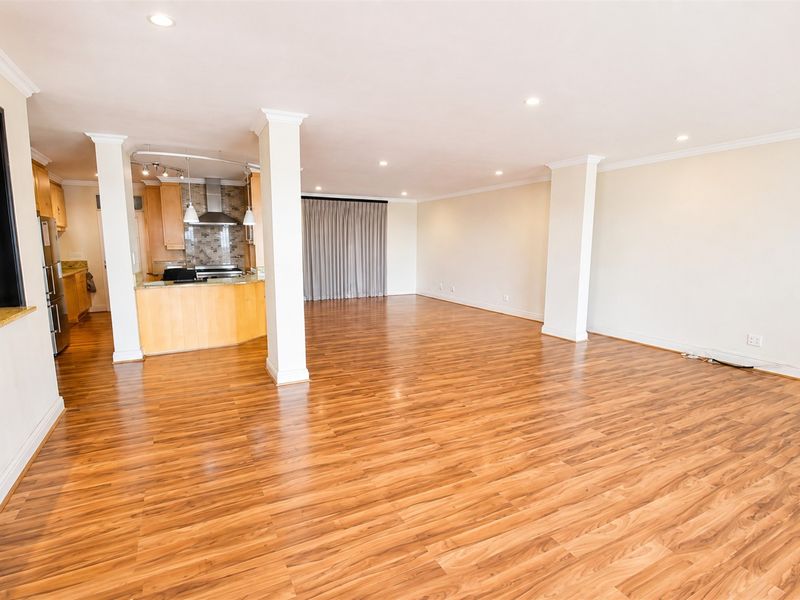 Spacious open-plan living and kitchen area featuring warm laminate flooring, recessed lighting, crown molding, and a functional kitchen with granite countertops.
