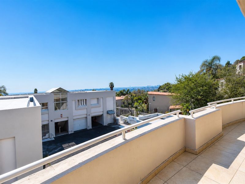 A spacious balcony featuring tiled flooring and a metal balustrade, offering elevated views of the surrounding neighborhood and distant landscape.