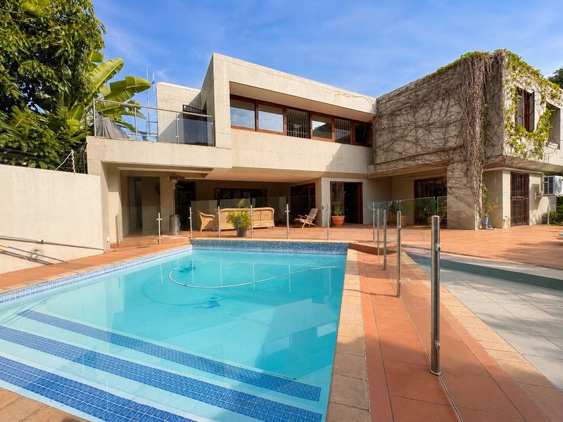 Spacious rear exterior featuring a swimming pool with glass fencing, a tiled patio area, and a multi-level architectural facade with climbing greenery.