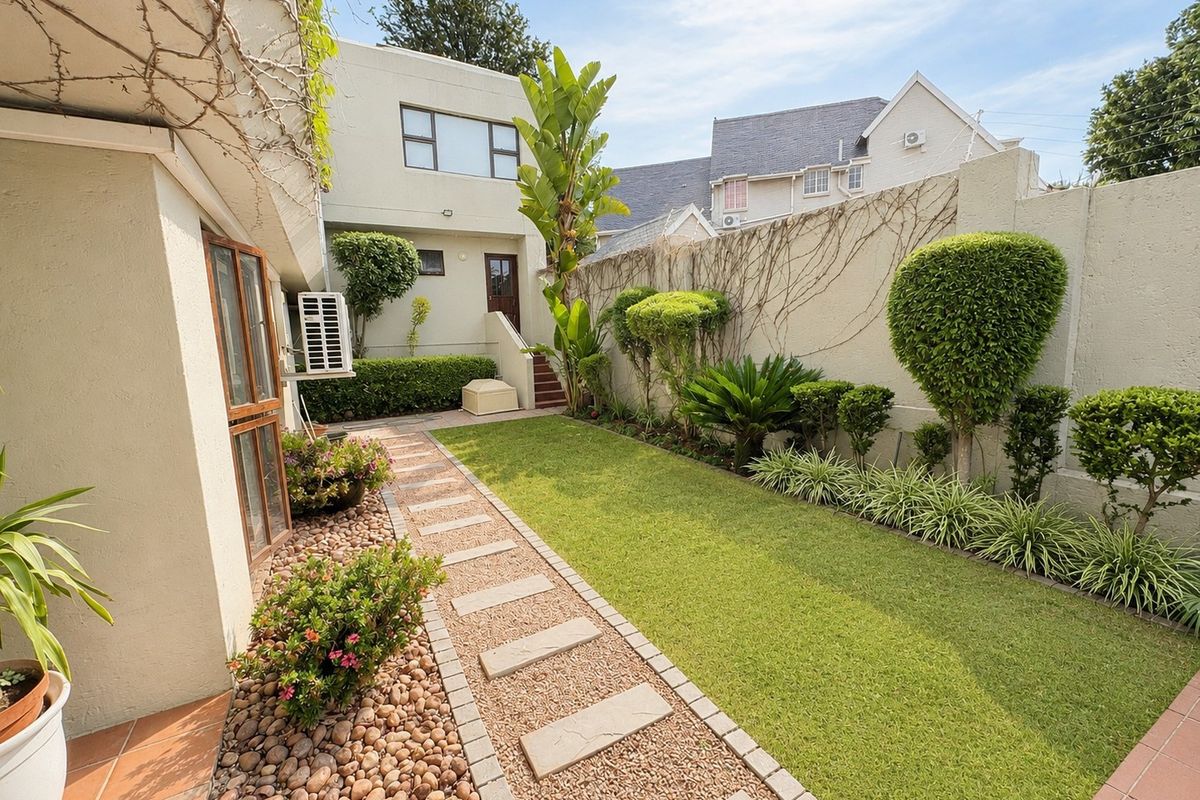 A well-maintained rear garden featuring a manicured lawn, stone pathway, and established perimeter landscaping with a private exterior staircase.