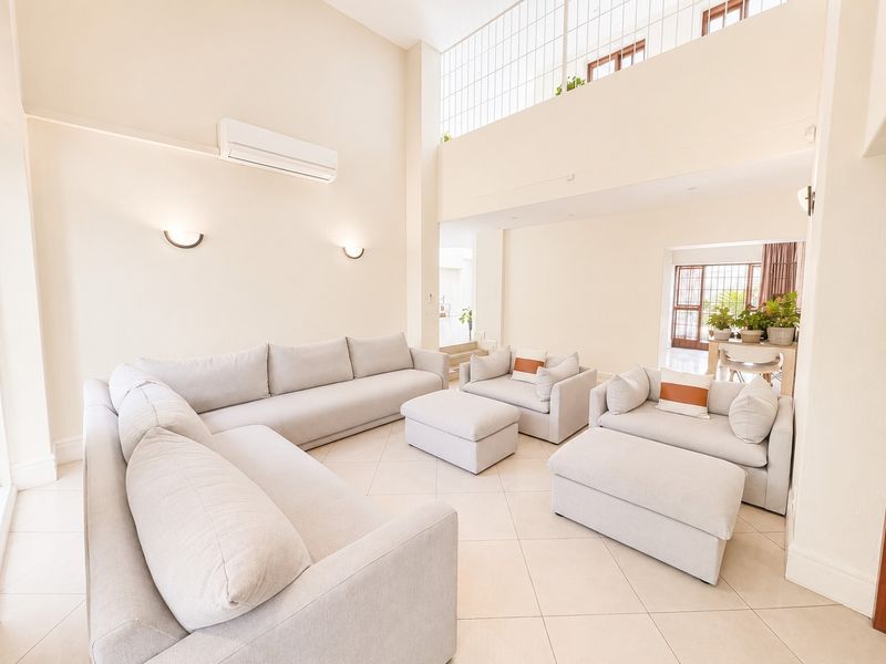 Spacious double-volume living area featuring tiled flooring, wall-mounted air conditioning, and a mezzanine level with a metal balustrade overlooking the space.