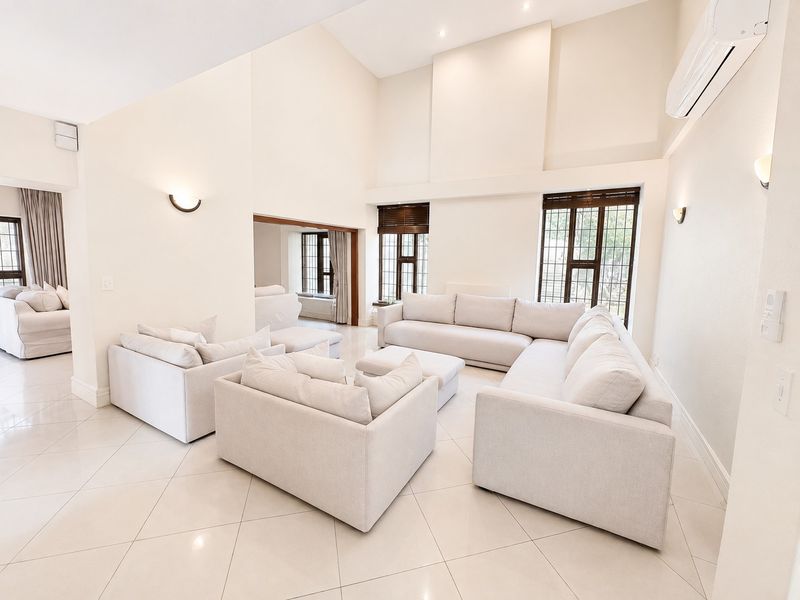 Spacious living room featuring high vaulted ceilings, large windows, tiled flooring, and a wall-mounted air conditioning unit in a bright, neutral setting.