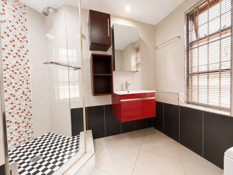A modern bathroom featuring a glass shower enclosure, a vibrant red wall-mounted vanity, and a striking mosaic tile feature wall.