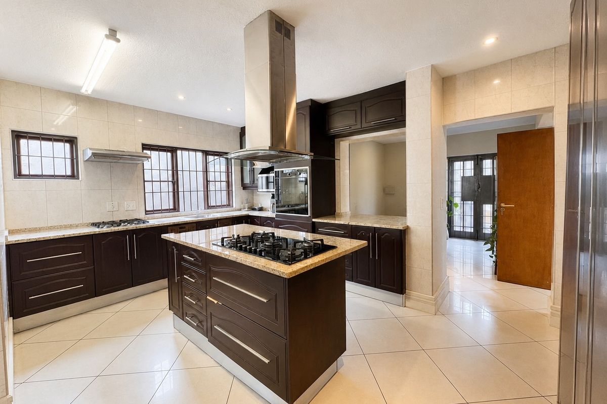 Spacious kitchen featuring a central island with a gas hob, granite countertops, dark cabinetry, and tiled flooring throughout.