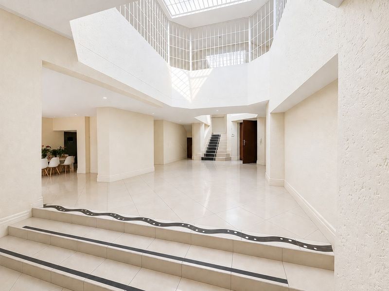 Spacious, light-filled entrance hall featuring high ceilings with a large skylight, tiled flooring, and a central staircase leading to the upper level.