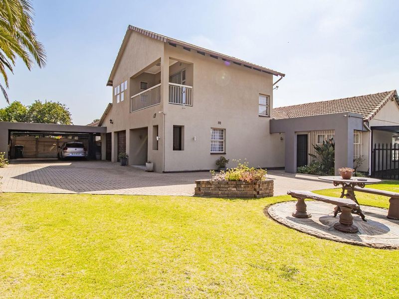 A well-maintained double-story residential property featuring a paved driveway, integrated carport, balcony, and a landscaped front garden area.