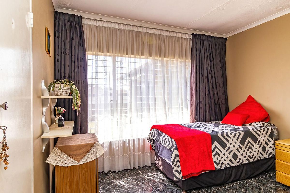 A functional bedroom featuring tiled flooring, a built-in cupboard, and large windows fitted with security bars for added safety.