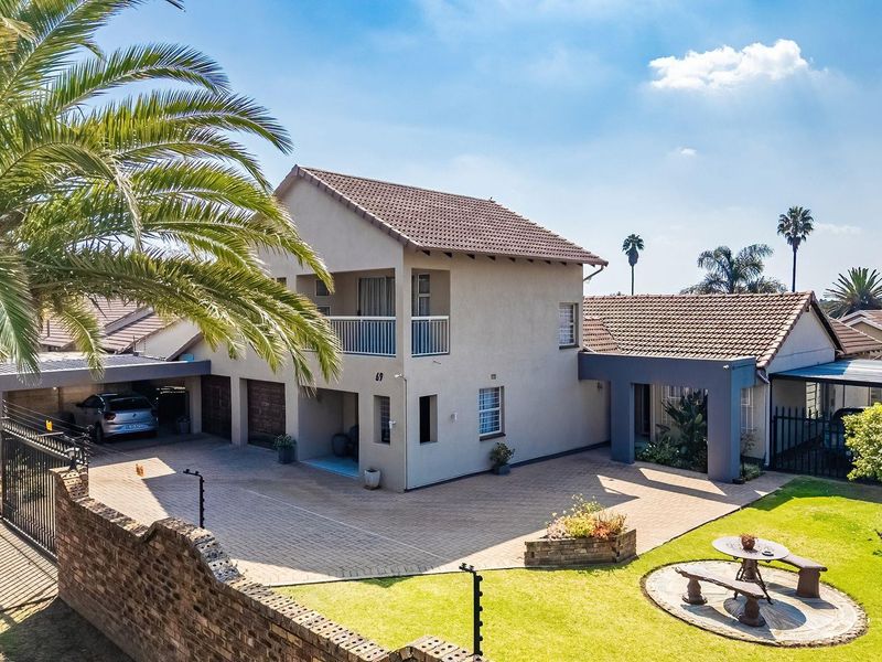 An elevated view of a well-maintained double-story residential property featuring a paved driveway, double garage, carport, and a landscaped front garden.