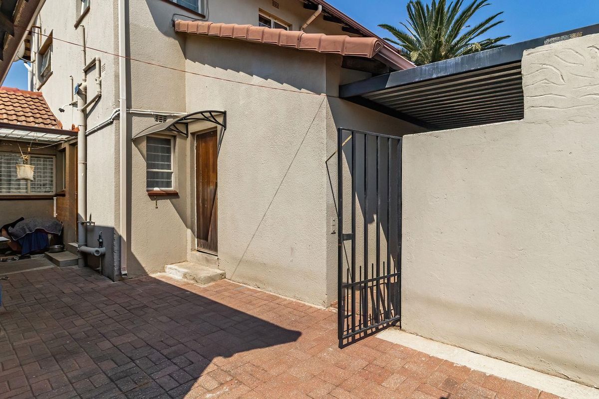 A paved rear courtyard area featuring a metal security gate, external access door, and covered section, providing functional outdoor space.