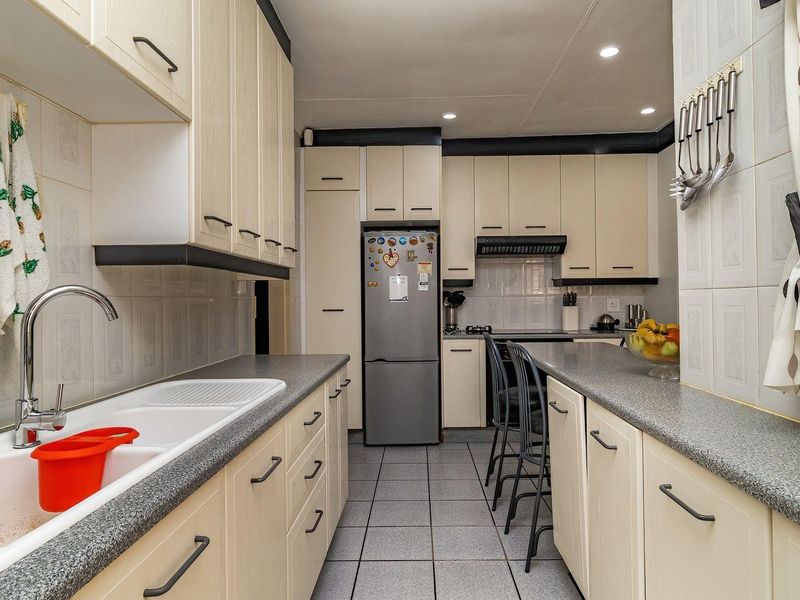 A functional galley-style kitchen featuring ample built-in cabinetry, laminate countertops, a double sink, and tiled finishes throughout.