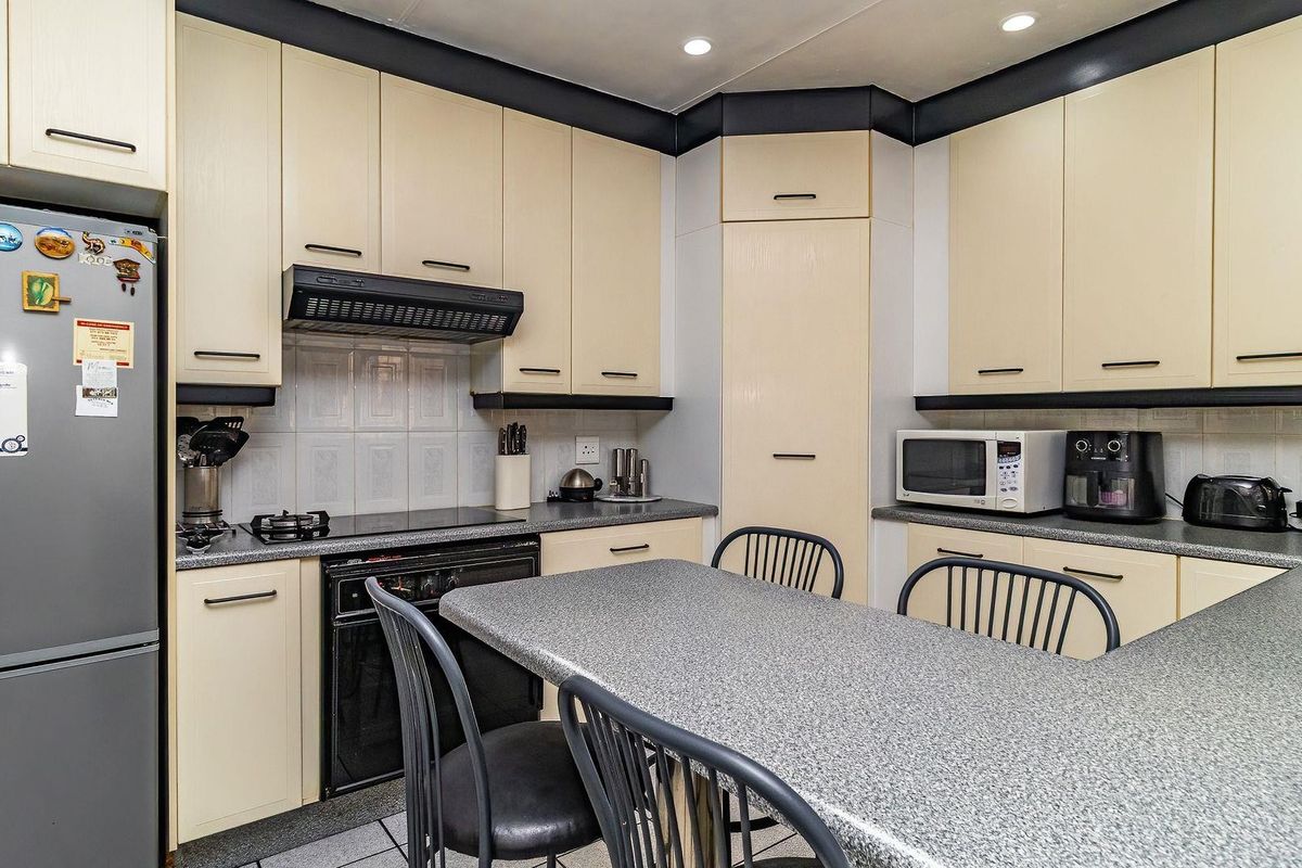 A functional kitchen featuring light-toned cabinetry, dark contrasting trim, laminate countertops, and integrated appliances including an oven and extractor fan.