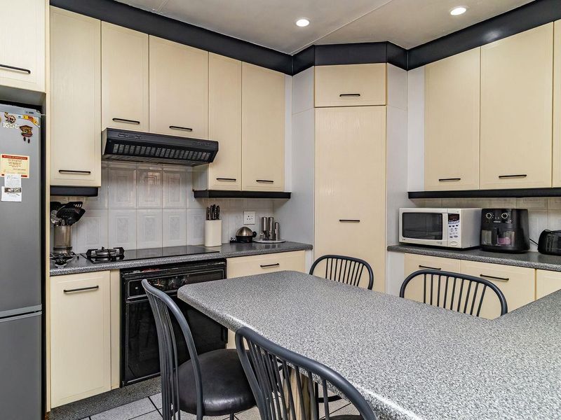A functional kitchen featuring light-toned cabinetry, dark contrasting trim, laminate countertops, and integrated appliances including an oven and extractor fan.