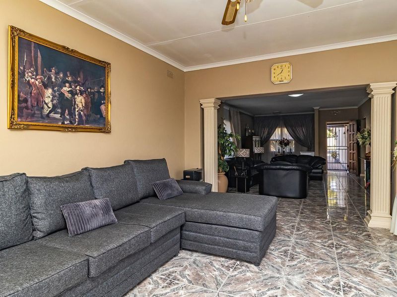 Spacious living area featuring tiled flooring, decorative columns, and a coved ceiling, providing an open-plan feel with access to an adjacent room.