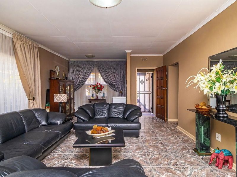 A spacious living room featuring tiled flooring, neutral wall tones, and a security gate leading to an adjacent area.