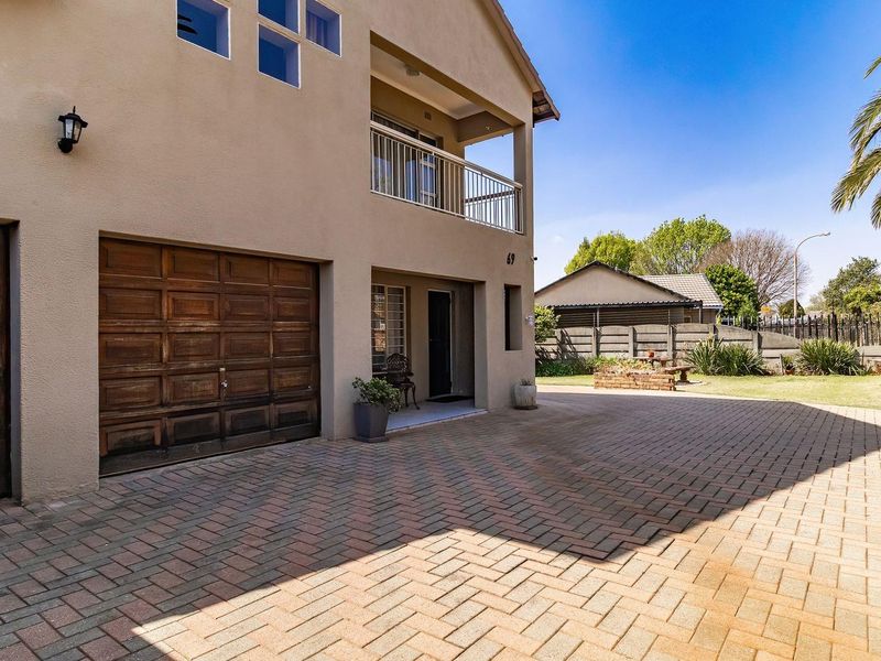 Front exterior view featuring a paved driveway, wooden garage door, and an upper-level balcony with metal railings.