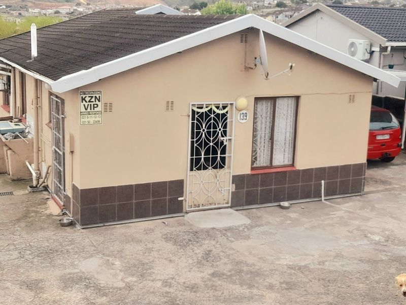 Front elevation of a single-story house featuring a tiled roof, security gate, and external wall tiling, with a concrete driveway area.
