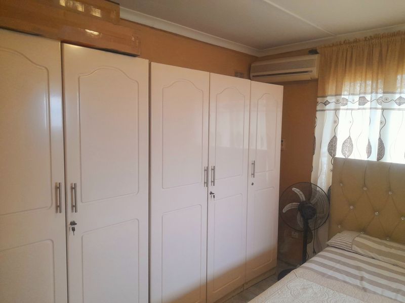 A bedroom featuring white built-in cupboards and a wall-mounted air conditioning unit.