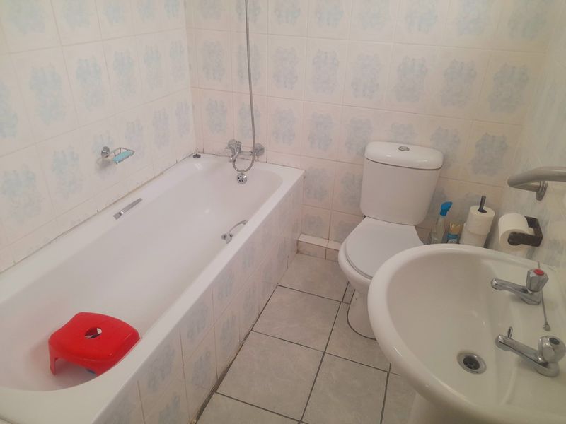 A functional bathroom featuring a standard bathtub, pedestal sink, and toilet with dated wall tiling and ceramic floor finishes.