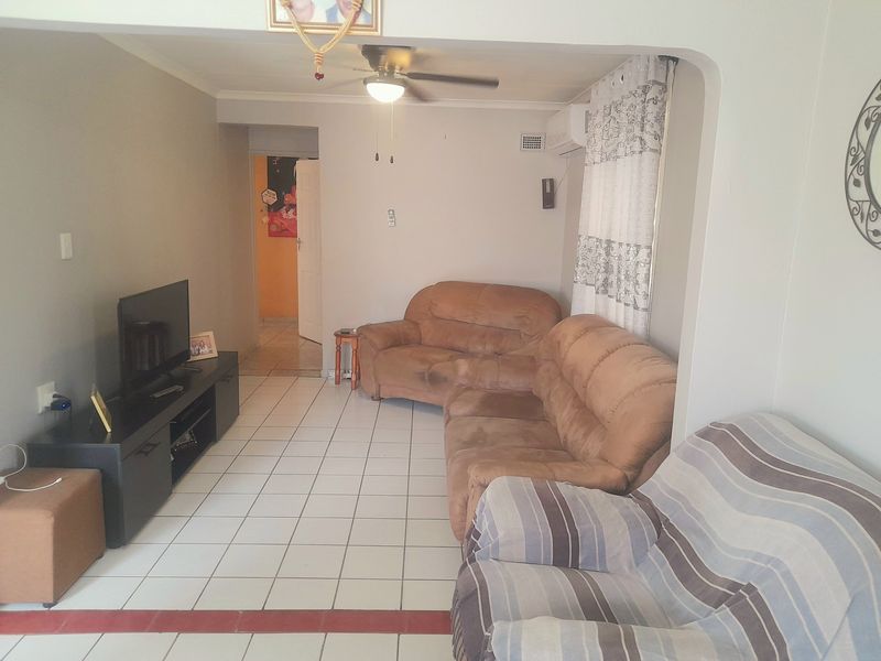 A living room featuring ceramic floor tiles, a ceiling fan, and a wall-mounted air conditioning unit.