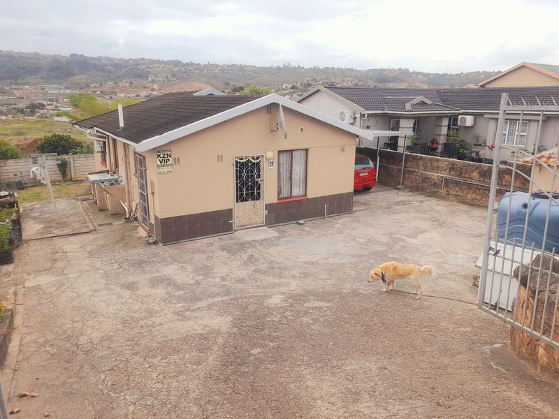 Front exterior view of a detached house featuring a concrete driveway, security gate, and tiled roof, set against a hillside landscape.