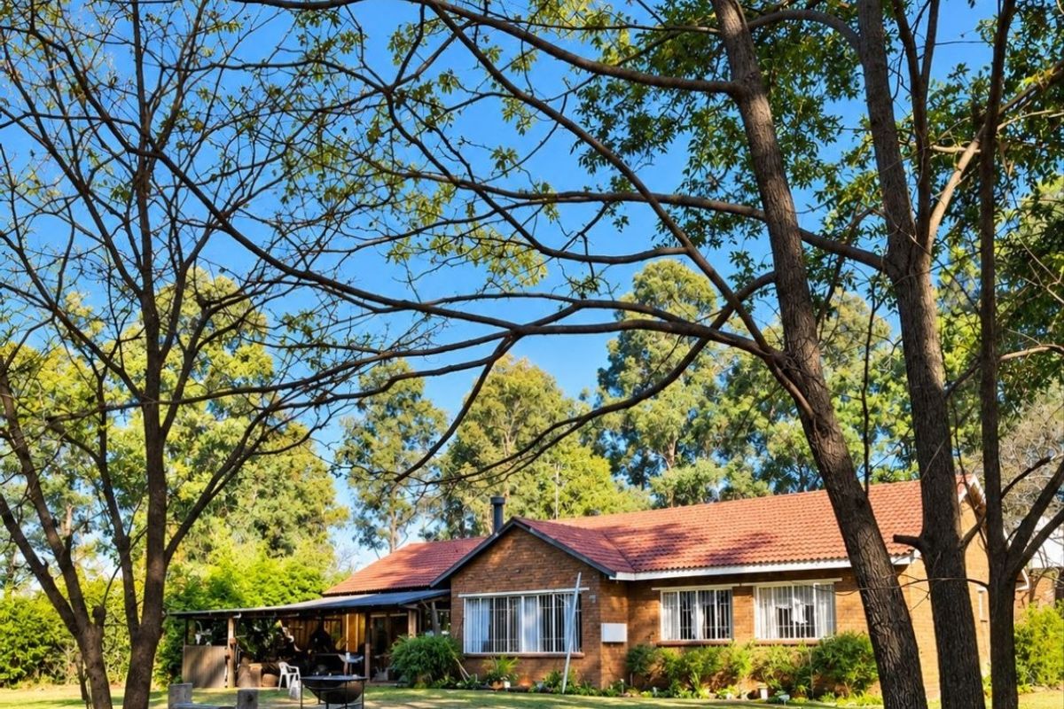 A view of the rear brick farmhouse elevation featuring a tiled roof, security bars on windows, and a covered patio area set within a garden.