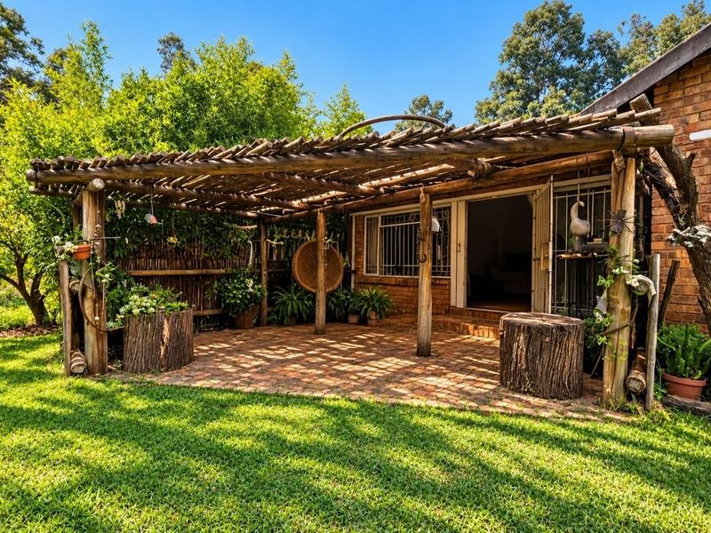 A rustic outdoor patio area featuring a timber pergola structure and brick paving, providing a shaded transition space between the garden and the home.