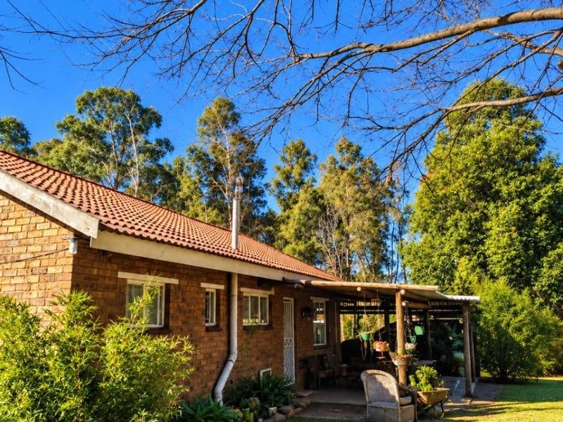 Rear view of a brick farmhouse featuring a covered patio area with timber pergola, set within a spacious garden with mature trees.