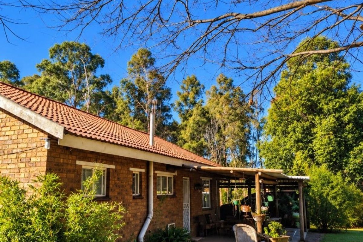 Rear view of a brick farmhouse featuring a covered patio area with timber pergola, set within a spacious garden with mature trees.