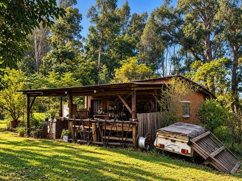 A rustic outdoor structure with a corrugated metal roof and timber framing, situated in a lush, tree-lined farm setting.