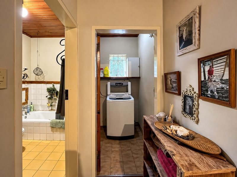 A view from the hallway looking into a bathroom and a small laundry area with tiled floors and timber ceiling accents.