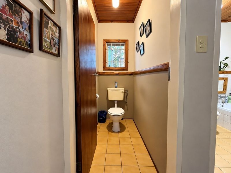 A compact bathroom featuring ceramic tile flooring, a timber-paneled ceiling, and a timber-framed window with security bars.