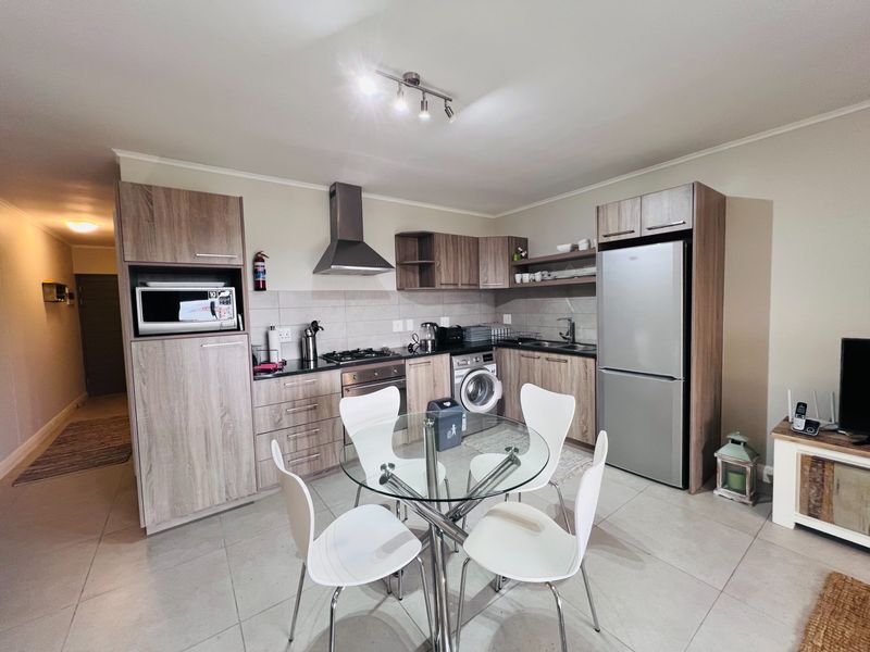 Modern open-plan kitchen featuring wood-finish cabinetry, integrated appliances, gas hob, and tiled flooring, seamlessly flowing into the dining and living area.