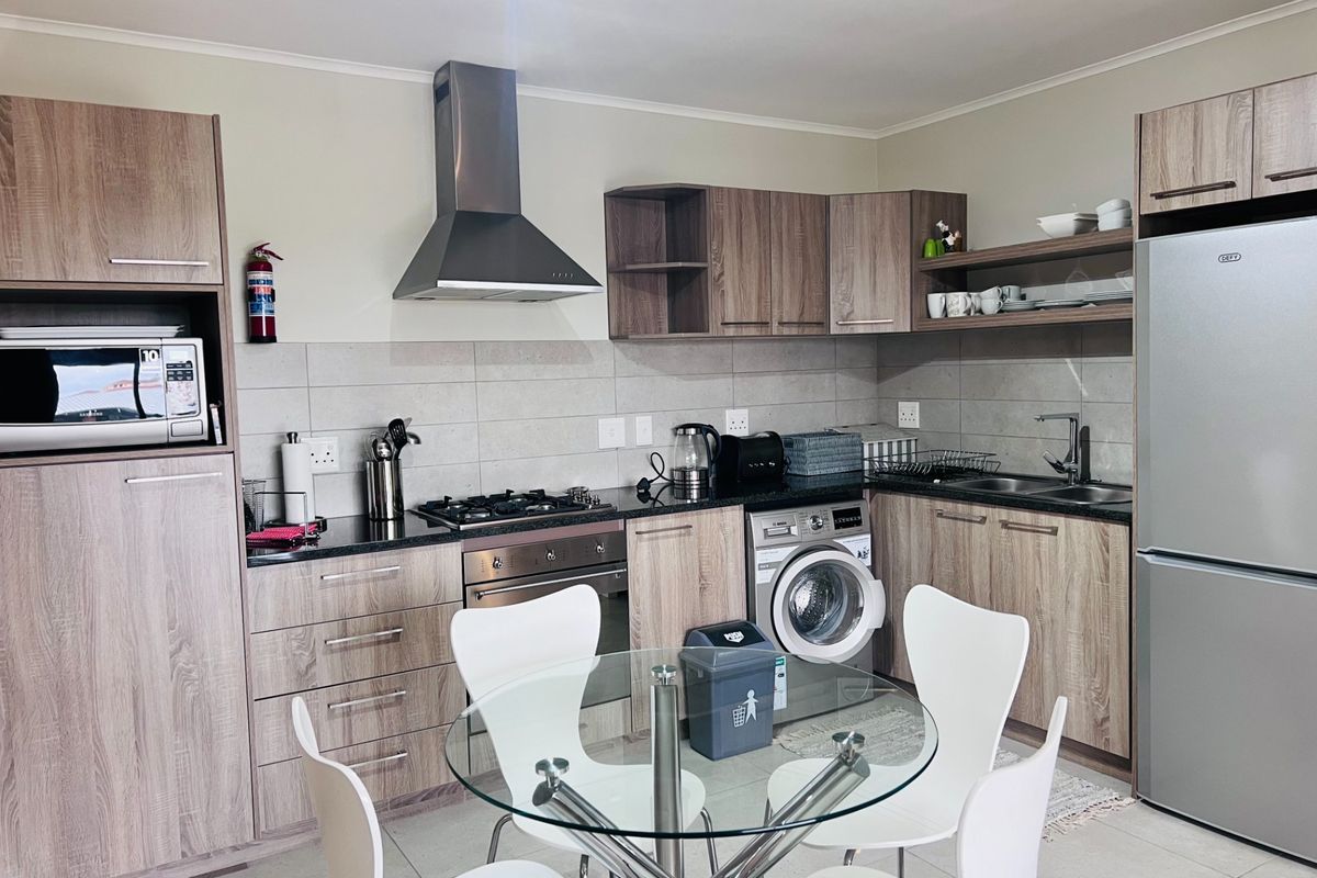 Modern kitchen featuring wood-finish cabinetry, granite countertops, gas hob, electric oven, stainless steel extractor fan, and an integrated washing machine.