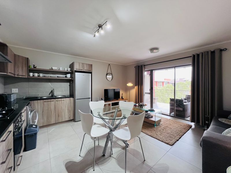 An open-plan living and kitchen area featuring modern cabinetry, stone countertops, tiled floors, and direct access to a private balcony through sliding glass doors.